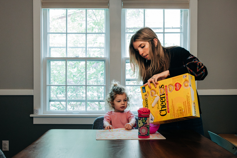 mother pours Cheerios for daughter sitting at the dining room table
