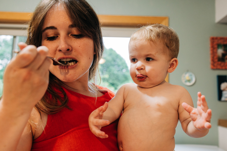 mom takes a bite of food while toddler boy sticks out tongue in anticipation