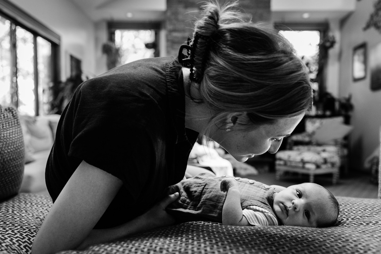 mother looks at newborn baby while baby makes eye contact with camera